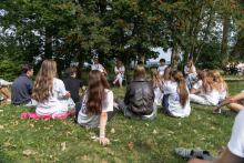 Outdoor discussion group seated on the grass beneath trees at a student event.