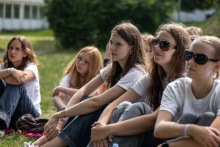 Kilka uczestniczek siedzi na trawie i uważnie słucha prowadzonej rozmowy lub prezentacji.