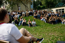 Participants seated on a grassy slope listening to a speaker during an outdoor workshop session.