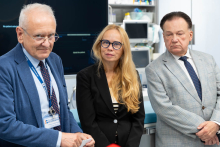 Three people attend a presentation of new medical equipment in a hospital procedure room. Diagnostic devices are visible in the background. Zdjęcie 2 PL: Sala zabiegowa wyposażona w nowoczesny angiograf, monitor medyczny oraz stanowiska do monitorowania pacjenta. Widoczne jest oznakowanie Szpitala Bródnowskiego. EN: Procedure room equipped with a modern angiography system, medical monitor and patient monitoring stations. Signage of Brodnowski Hospital is visible. Zdjęcie 3 PL: Lekarz udziela wywiadu mediom 