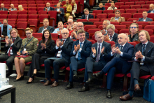 Conference attendees seated in the front rows of an auditorium applaud during a conference session.