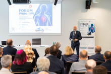 A speaker addresses attendees at the WUM-PW Forum. A screen displays the event program focused on health technologies.