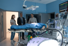 Kobieta oraz dwóch mężczyzn stoją przy stanowisku symulującym salę operacyjną. Na stole operacyjnym leży fantom pacjenta podłączony do aparatury medycznej.
