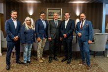 Group portrait of six participants standing together in a meeting room during an official visit.