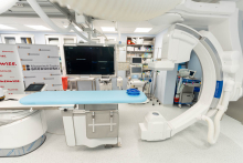View of an interventional procedure room with an angiography system, diagnostic monitor, and medical procedure table.