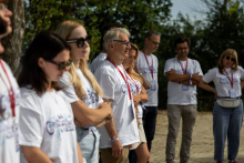 Grupa organizatorów, kobiet i mężczyzn w białych koszulkach oraz identyfikatorach, stoi podczas spotkania na świeżym powietrzu.