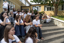 Uczestniczki wydarzenia siedzą na schodach i słuchają wystąpienia. W tle znajdują się kolejne grupy słuchaczy.