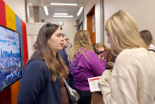 Osoba reprezentująca Warszawski Uniwersytet Medyczny rozmawia z odwiedzającą przy stoisku uczelni. W tle widoczne są inne osoby oraz ekran prezentacyjny.