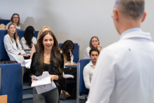 Studentka podchodzi z białym fartuchem do przedstawiciela uczelni podczas ceremonii.