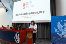 Kobieta stoi przy mównicy z napisem „Veritatis Splendor” i przemawia podczas Dnia Adaptacyjnego Wydziału Lekarsko-Stomatologicznego. Za nią siedzą kobieta i mężczyzna, a na ekranie wyświetlony jest tytuł wydarzenia.