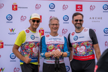 Three participants pose for a photo in front of a sponsor backdrop at the “Run for New Life” event. Two participants hold Nordic walking poles.