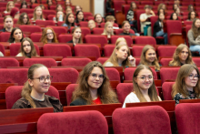 Uczestnicy siedzą w rzędach czerwonych foteli i słuchają wystąpień odbywających się na scenie.