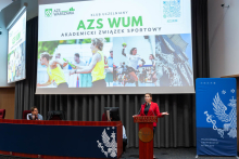 Kobieta stoi przy mównicy z napisem „Veritatis Splendor” i prezentuje działalność AZS WUM. Za nią wyświetlony jest slajd poświęcony Akademickiemu Związkowi Sportowemu.