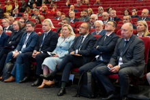 Uczestnicy konferencji siedzą w audytorium i słuchają prezentacji. Kilka osób trzyma materiały konferencyjne.