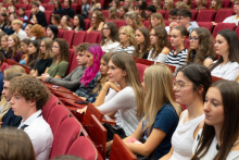 Uczestnicy siedzą w rzędach czerwonych foteli i słuchają wystąpień podczas wydarzenia.