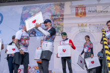 Several participants stand on a stage during a ceremony held as part of the “Run for New Life” event. The participants hold framed artworks featuring a heart motif.