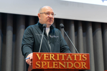 Mężczyzna przemawia przy mównicy z napisem „Veritatis Splendor” podczas spotkania inaugurującego rok akademicki.