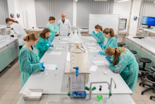 Grupa uczestników wykonuje doświadczenia przy stanowiskach laboratoryjnych pod nadzorem prowadzącego.