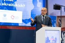 Jedna osoba przemawia z mównicy podczas konferencji. W tle znajduje się ekran prezentacyjny z informacjami o wydarzeniu.