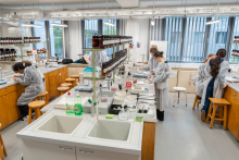Szeroki widok laboratorium z uczestnikami pracującymi przy stołach wyposażonych w sprzęt laboratoryjny i odczynniki.