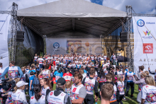 Uczestnicy wydarzenia zgromadzili się przed sceną do wspólnego zdjęcia. Na scenie stoi liczna grupa osób w koszulkach „Biegu po Nowe Życie”, a wokół znajdują się przedstawiciele mediów i pozostali uczestnicy.