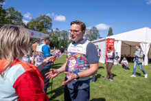 One participant speaks to a reporter holding a microphone during the “Run for New Life” event. Other participants and an event tent are visible in the background.