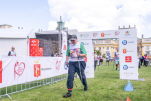 A participant using Nordic walking poles walks along the event route marked with sponsor banners. Other participants and the event arch are visible in the background.