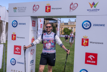 A participant with Nordic walking poles stands beneath an event arch on the route of the “Run for New Life” event.