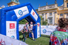 An adult participant and a child pass through the finish arch of the “Run for New Life” event. Event staff and participants stand alongside the route.