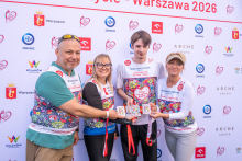 Four people pose for a photo in front of the event backdrop. Three participants display commemorative medals on red ribbons.