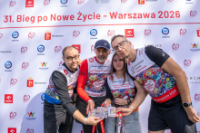 Four people pose for a photo in front of the event backdrop. The participants display commemorative medals.