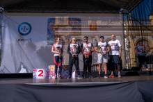 Five people stand on stage during an award ceremony. The participants hold trophies, and a podium and additional awards are visible nearby.