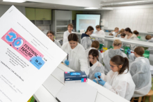 Uczestnicy zajęć laboratoryjnych wykonują ćwiczenia przy stanowiskach. Na pierwszym planie znajduje się karta z materiałami do zajęć Festiwalu Nauki.