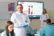 Prowadzący omawia tematykę badań krwi podczas zajęć. W tle widoczna jest prezentacja multimedialna.