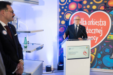 The Rector of the Medical University of Warsaw speaks at a lectern during a ceremony at the clinic. In the background, the Great Orchestra of Christmas Charity (WOŚP) logo and a screen displaying the name of the Department of Cardiac, Thoracic Surgery and Transplantology can be seen.