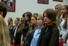 Grupa uczestników stoi wśród rzędów czerwonych foteli podczas uroczystości w audytorium.