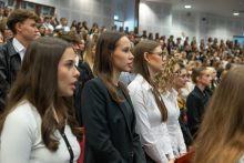 A group of ceremony participants stand among rows of red seats in an auditorium. 