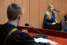 Kobieta w ciemnym garniturze przemawia za mównicą podczas symulacji rozprawy sądowej w auli przed publicznością i panelem jurorów.