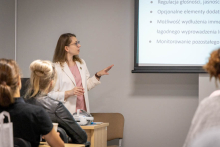 A woman is giving a presentation to workshop participants. She is pointing to a slide displayed on a screen.