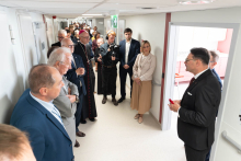 A group of event participants stand in a hospital corridor. One person gives a presentation about the ward while the others listen.