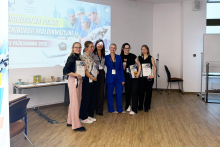 Six people pose for a group photo during the awards ceremony. Some participants are holding certificates, books, and a trophy.