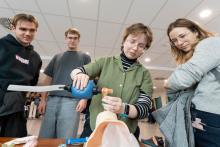 A person demonstrates how to ventilate a manikin using a bag-valve mask. Three people watch the demonstration.