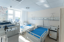 A hospital room with three patient beds. Medical installations and bedside cabinets are located next to the beds.