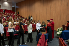 Uczestnicy podchodzą kolejno do przedstawicieli uczelni ubranych w ceremonialne togi akademickie.