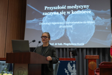 A person wearing a dark blazer and glasses gives a lecture at a lectern with two microphones. The slide displayed on the screen behind them reads: “The future of medicine begins in the cell. From regenerative biology and biomaterials to the therapies of the future.”