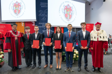Six people pose for a group photo holding documents presented during the ceremony. University representatives stand on either side of the group.