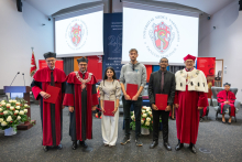 Three people pose for a group photo holding documents presented during the ceremony. University representatives stand on either side of the group.