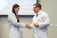 Two people wearing white coats shake hands during the ceremony.