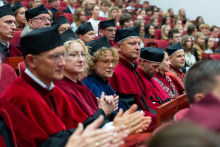 Participants wearing academic gowns sit in the auditorium and listen to the proceedings of the academic year inauguration ceremony.