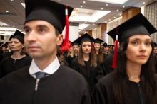 A large group of people in black academic gowns and mortarboards stand in the hall during an academic ceremony.